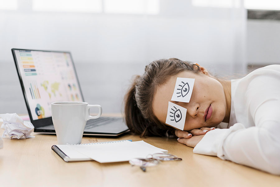 woman sleeping at desk with post it notes covering her eyes with eyes drawn on them
