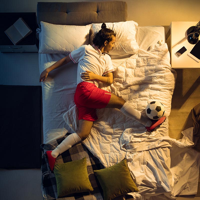 sleeping boy in bed wearing soccer uniform kicking soccer ball