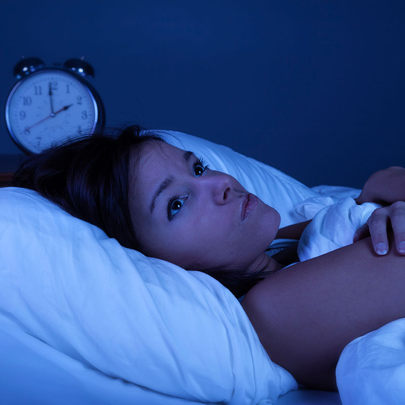 woman unhappy and awake in bed with a clock showing a time of two in the morning