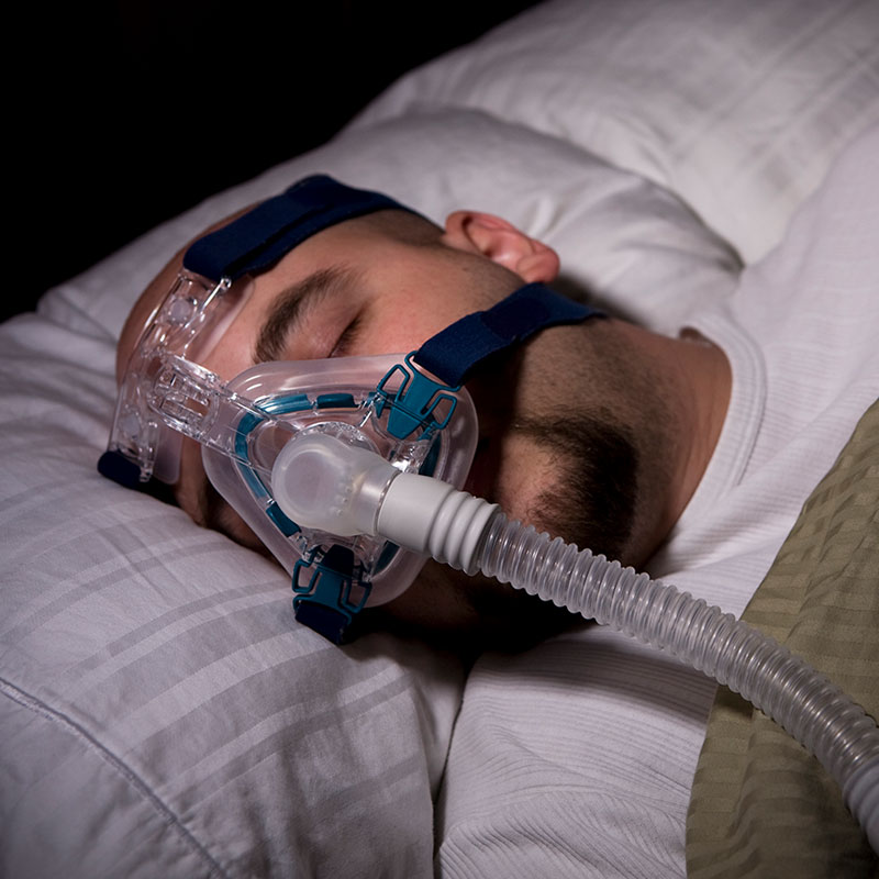 man sleeping in bed with CPAP machine on his face